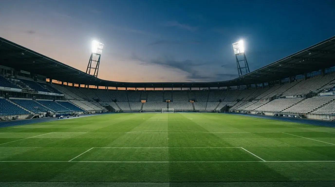 Een leeg voetbalstadion met lichtmasten bij schemering