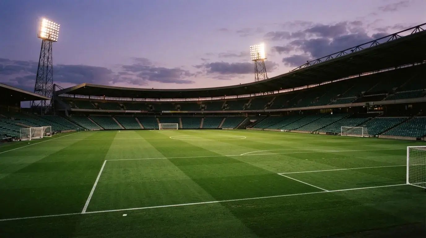 Een leeg voetbalstadion met lichtmasten bij schemering